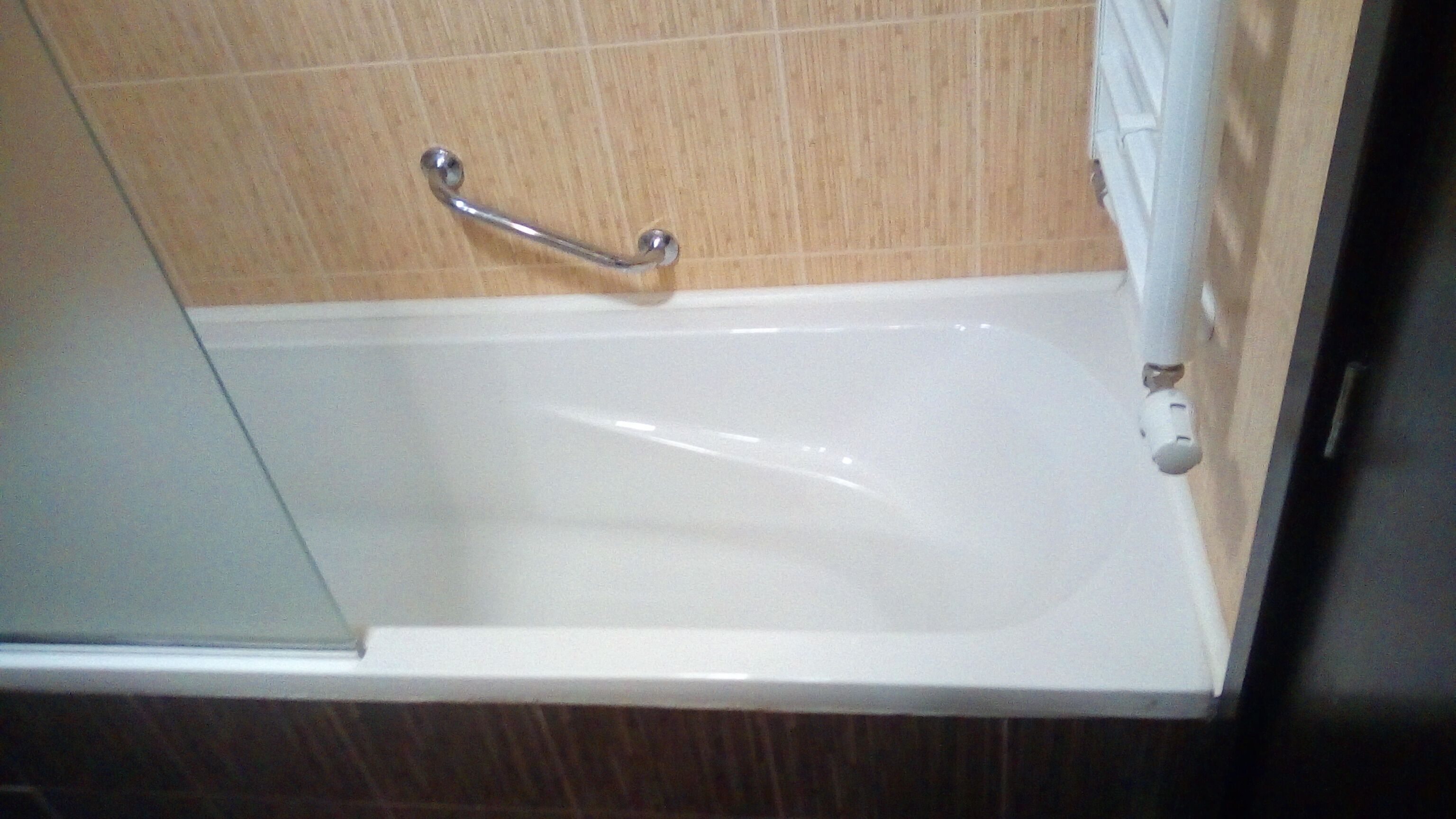 A bathtub with a grab bar, a white towel, and a wooden floor.