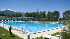 A rectangular swimming pool with a clear blue water surface, surrounded by a tiled deck. In the background, there are trees and a mountain range.