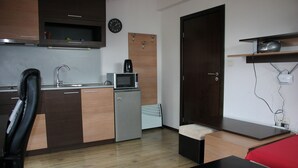 A compact kitchen with a microwave, coffee maker, and a small refrigerator. There is a wooden door, a black chair, and a red sofa in the living area.
