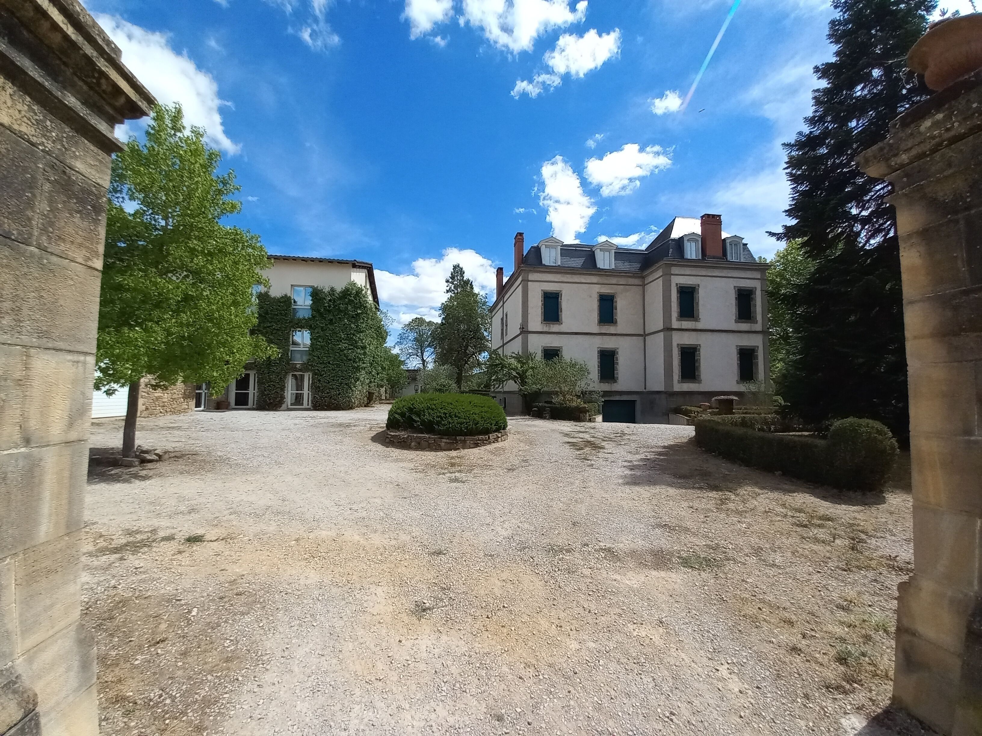 A courtyard with a gravel ground, surrounded by buildings with stone walls and large windows.