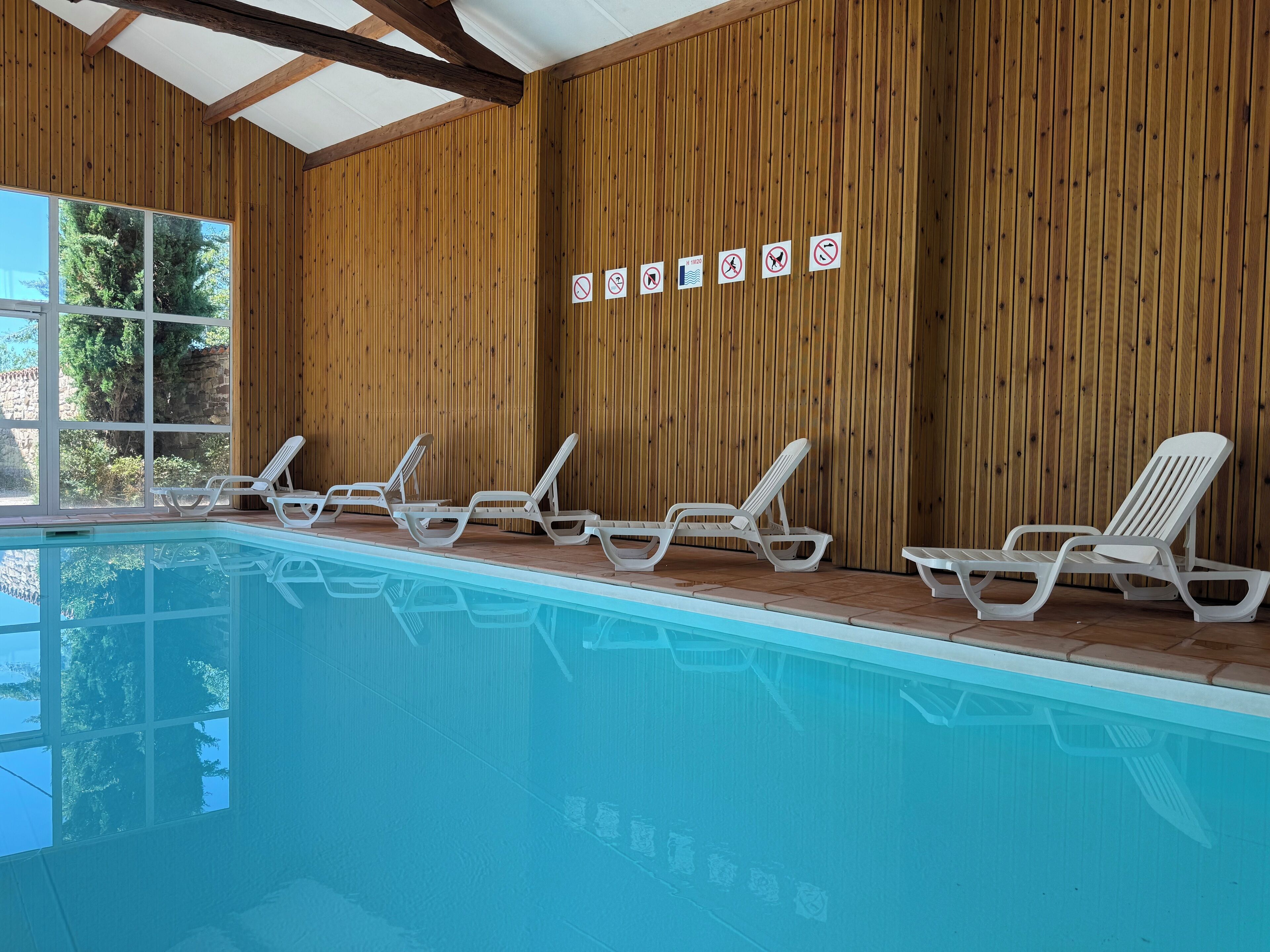 Une piscine intérieure avec des murs en bois et des chaises longues blanches.