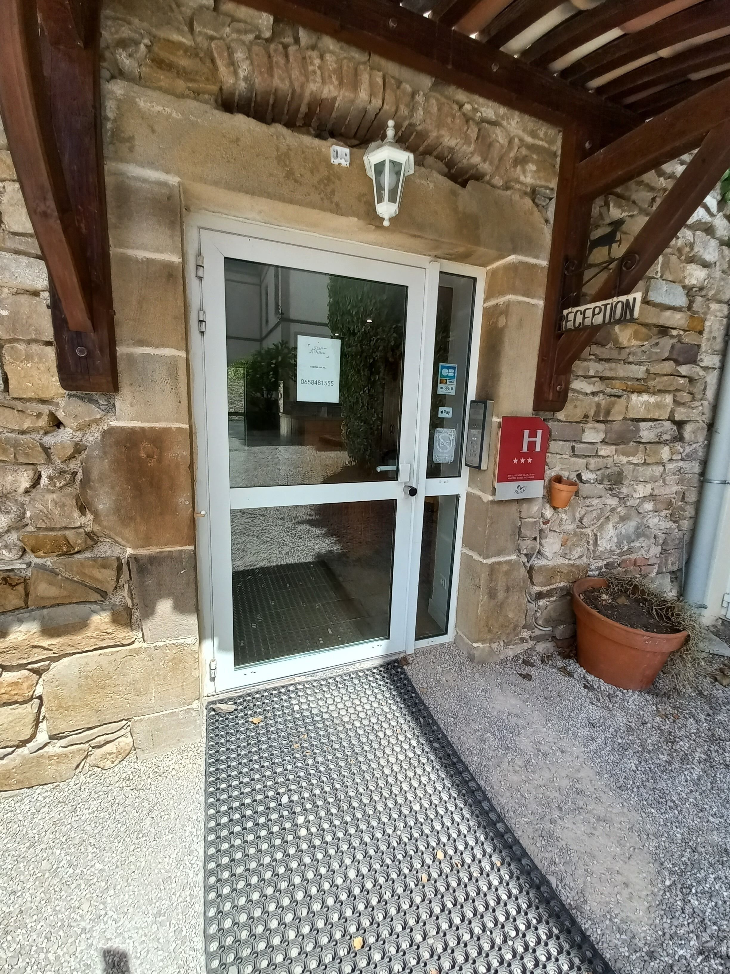 A hotel entrance with a stone facade, a reception area, and a small potted plant.
