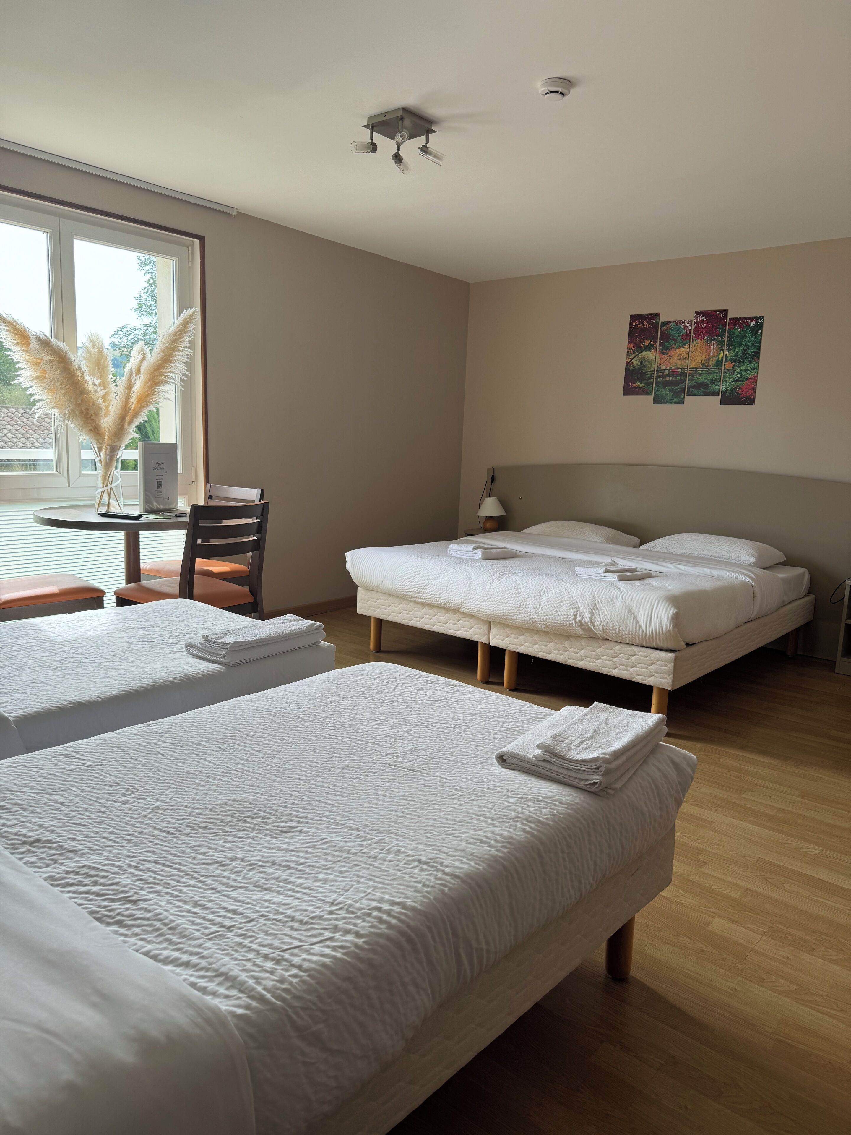 Une chambre d’hôtel avec deux lits, un bureau avec une chaise, une fenêtre donnant sur un paysage agréable et un ventilateur de plafond.