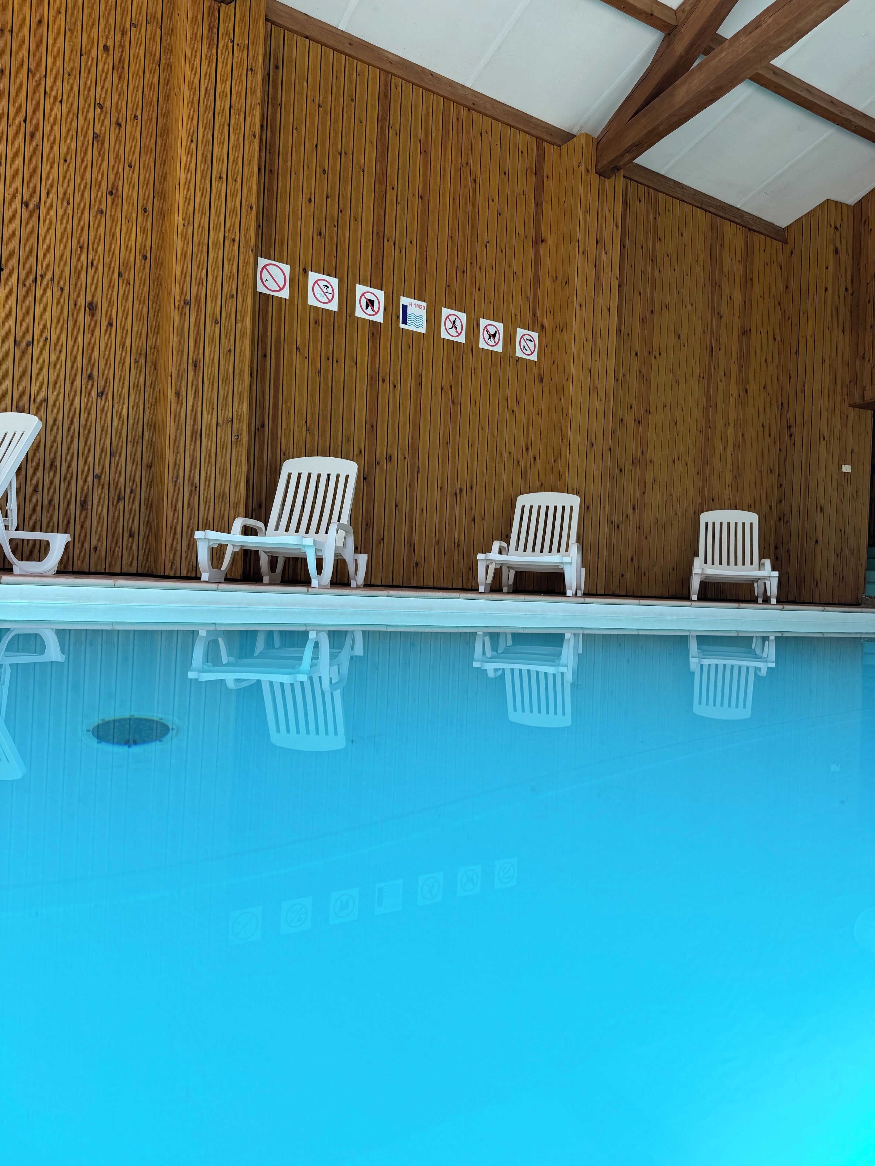 A swimming pool with white lounge chairs and wooden panel walls with no visible windows.