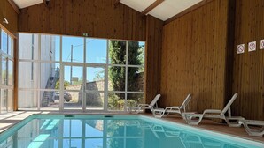 An indoor swimming pool with wooden beams, clear glass windows, and lounge chairs. - Hôtel La Métairie (Cordes-sur-Ciel)
