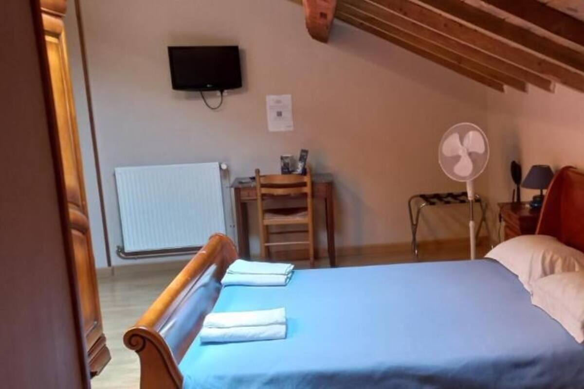 A bedroom with a bed, wooden headboard, bedside table, lamp, and a wall-mounted TV.