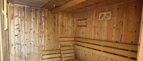 Eine Holzhütte als Sauna mit Bänken und einem kleinen Mülleimer.
