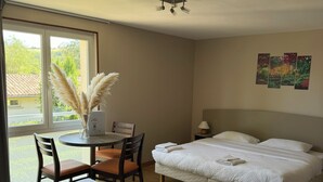 A hotel room with two beds, a dining table with chairs, a window with a view of greenery, and a ceiling fan. - Hôtel La Métairie (Cordes-sur-Ciel)