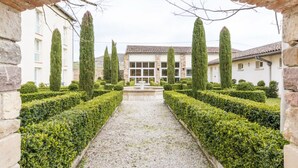 A formal garden with a gravel path, neatly trimmed hedges, and tall, cylindrical trees. - Hôtel La Métairie (Cordes-sur-Ciel)
