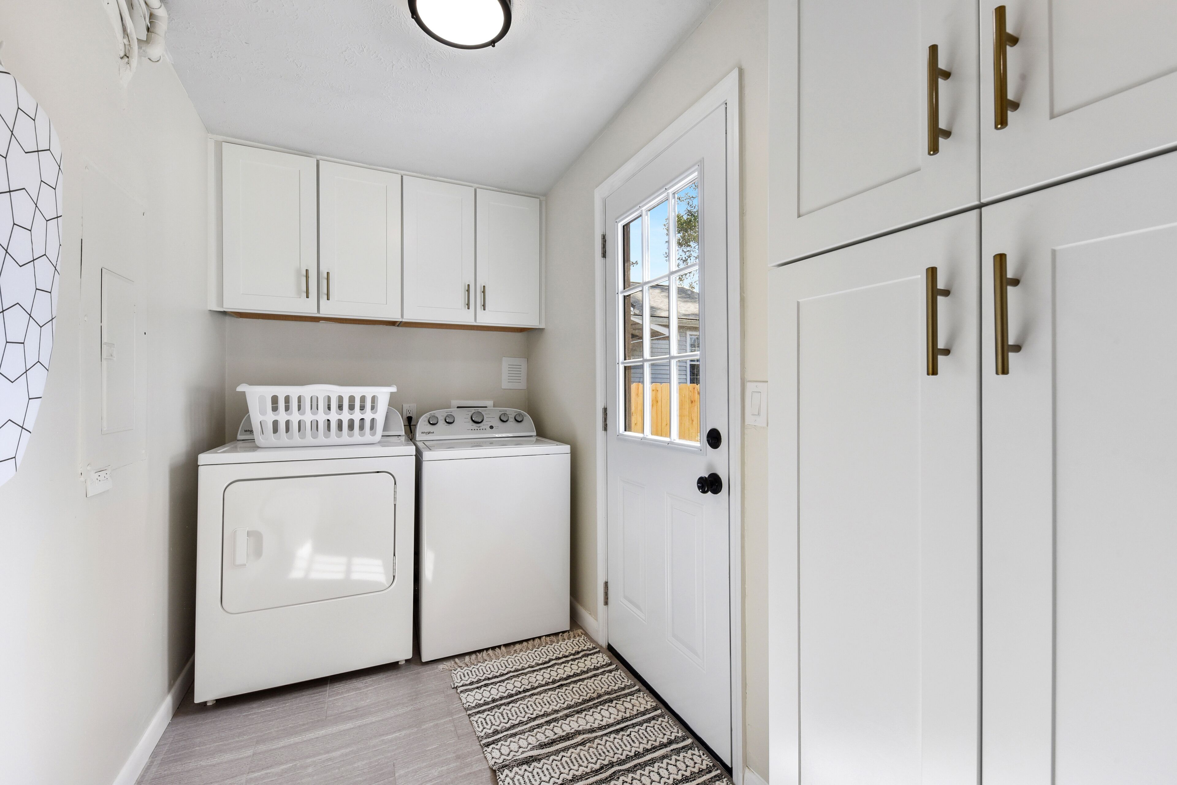 A laundry room with two white washing machines, a dryer, and white cabinets with gold handles.