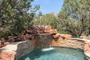 A swimming pool with a waterfall feature, surrounded by rocks and trees. - Best Iconic-Living Room Red Rock Views, Hot Tub, Borders The Forest (Sedona)