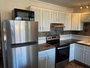 Una cocina con armarios blancos, un refrigerador de acero inoxidable, una estufa y un microondas.