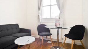 Ein Zimmer mit einem grauen Sofa, einem runden Tisch mit Marmorplatte und zwei schwarzen Stühlen.