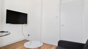 Ein Zimmer mit einem wandmontierten Flachbildfernseher, einem runden Tisch mit Marmorplatte und einem grauen Sofa.