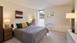 A bedroom with a bed, bedside tables, a dresser, a window, and a wall-mounted heater. - Charming 1-bed Apartment in Great Suffolk Street (London)