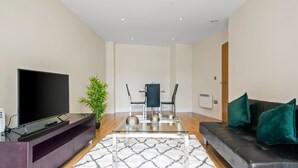 A modern living room with a flat-screen TV, a glass coffee table, a black leather sofa, and a dining area with a table and chairs. - Charming 1-bed Apartment in Great Suffolk Street (London)