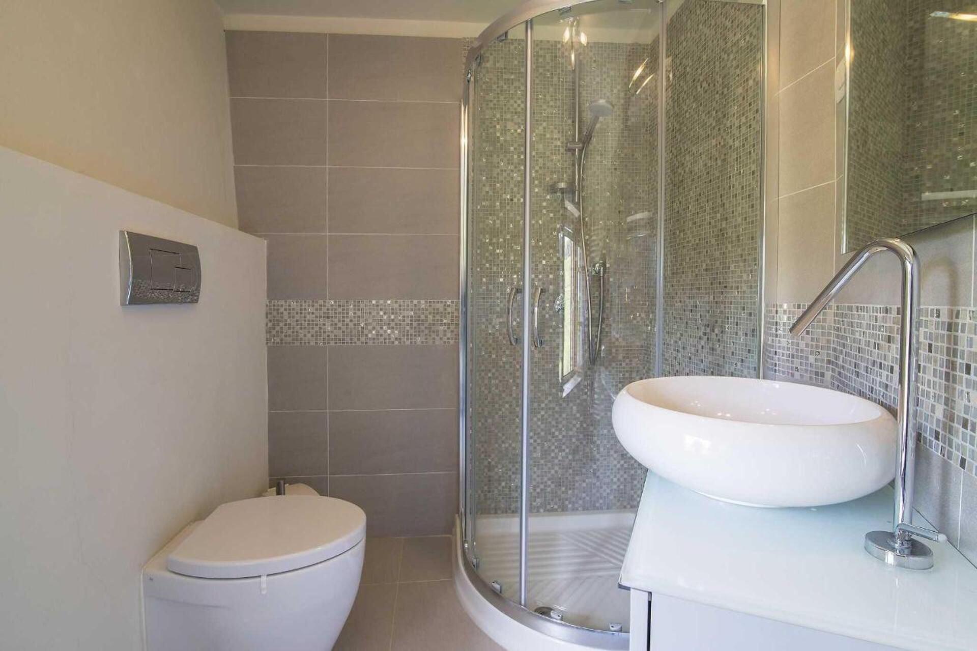 Ein Badezimmer mit einer gläsernen Duschkabine, einer weißen Toilette und einem weißen Waschbecken mit Spiegel.