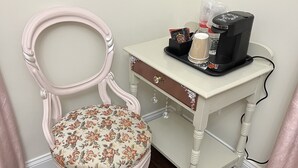 A chair with a floral cushion, a small white table with a drawer, and a coffee maker on the table. - Holland Farmhouse Inn B & B (Holland)