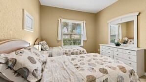 Une chambre avec deux lits, une commode, une fenêtre avec des stores et un tableau encadré au mur.
