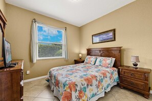 A bedroom with a bed, a nightstand, a dresser, a window with blinds, and a framed picture on the wall.