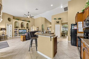 A spacious kitchen with a central island, a dining area with a TV, and a living room with bookshelves.