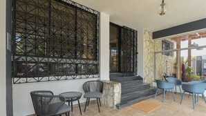 A covered outdoor seating area with a stone wall, metal gate, and blue chairs. - PH 19 Guesthouse Hotel in Gazcue (Santo Domingo)
