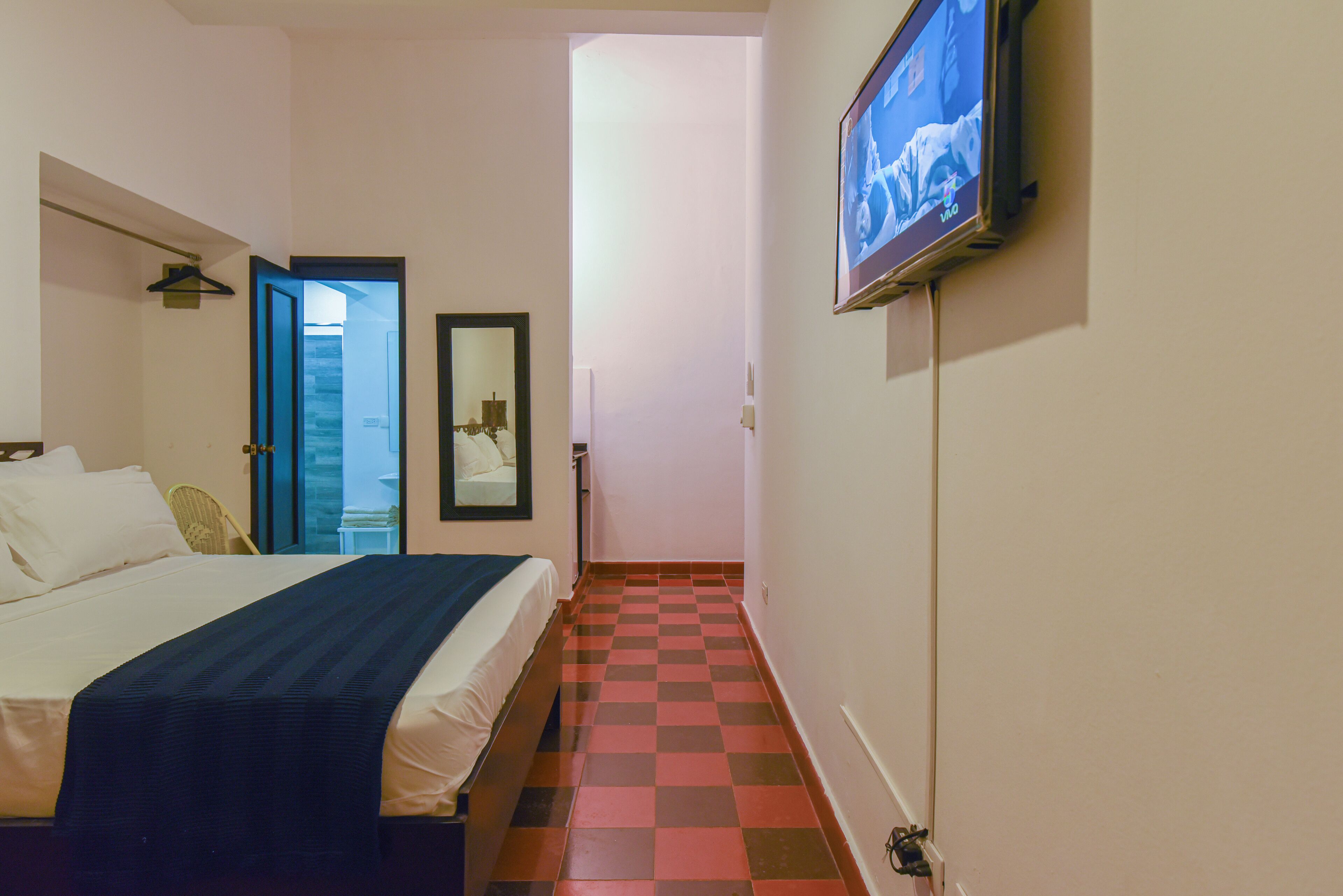 Una habitación de hotel con una cama, un televisor montado en la pared y un piso a cuadros.