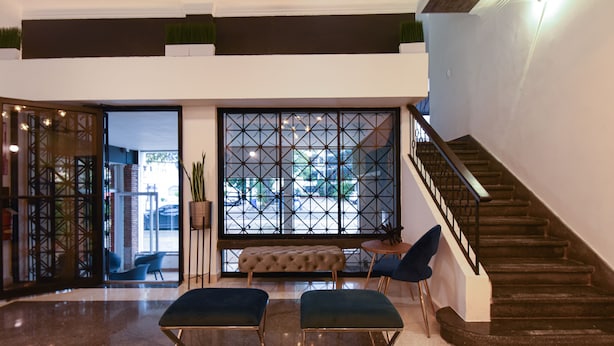 A spacious lobby with a staircase, a seating area with a tufted bench, and a large window with a geometric pattern. - PH 19 Guesthouse Hotel in Gazcue (Santo Domingo)