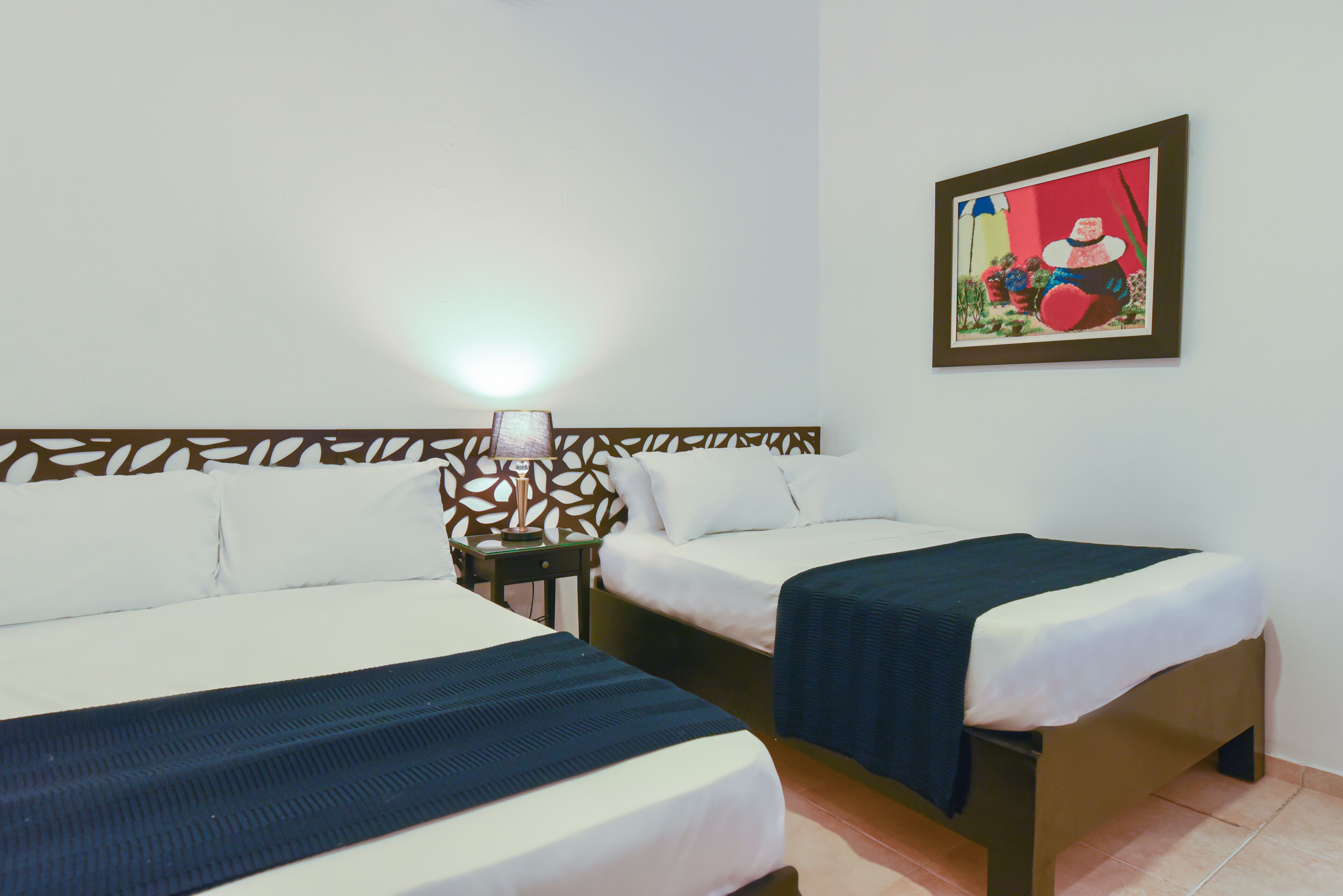 A hotel room with two beds, a nightstand with a lamp, a decorative wall panel, and a framed picture on the wall.