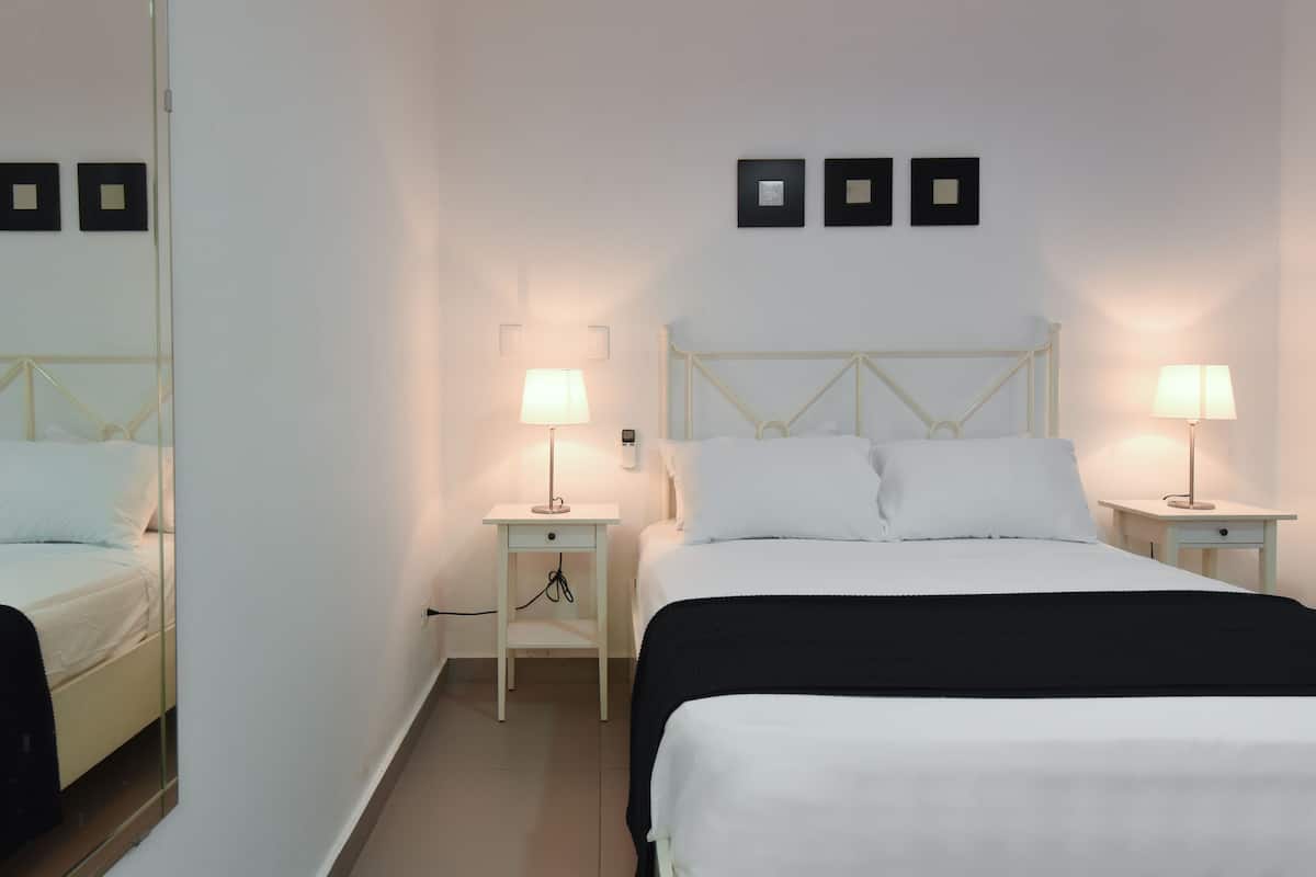 Ein Hotelzimmer mit einem Bett, zwei Nachttischen, einem Spiegel und drei gerahmten Bildern an der Wand.