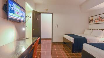 Habitación de hotel con televisor en la pared, escritorio, dos camas y piso de baldosas.