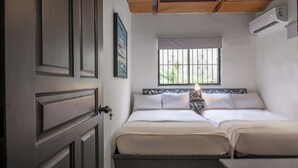 A room with two beds, a window with bars, a door, and an air conditioning unit. - PH 19 Guesthouse Hotel in Gazcue (Santo Domingo)