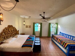 Quarto com duas camas, ventilador de teto e janela com cortinas verdes.