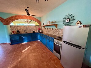 Uma cozinha com armários azuis, geladeira, fogão e um relógio decorativo na parede.