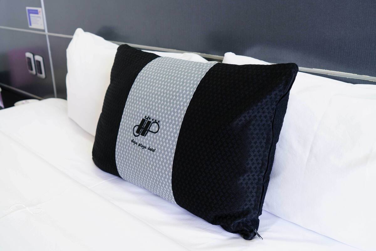 Un lit bien fait, avec un oreiller noir et blanc orné d’un logo et d’une inscription.