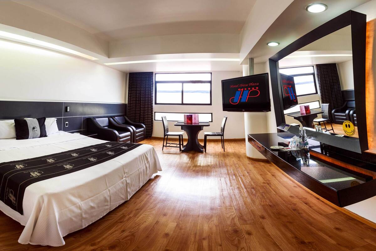 Une chambre d’hôtel avec un grand lit, un bureau avec une chaise, une télévision et un grand miroir.