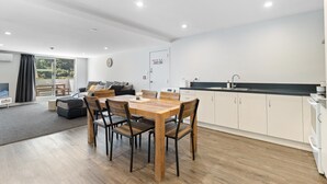 A modern kitchen with white cabinets, a black countertop, and a wooden dining table with chairs. - Central Mountain View Paradise (Queenstown)
