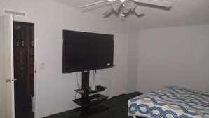 A room with a flat-screen TV mounted on the wall, a ceiling fan, a bed with patterned bedding, and a door leading to a closet. - Excellent Recreational Farm Minutes from DineyWorld (Frostproof)