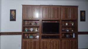 A wooden entertainment center with a flat-screen TV, shelves with decorative items, and a cabinet with a power outlet. - Excellent Recreational Farm Minutes from DineyWorld (Frostproof)