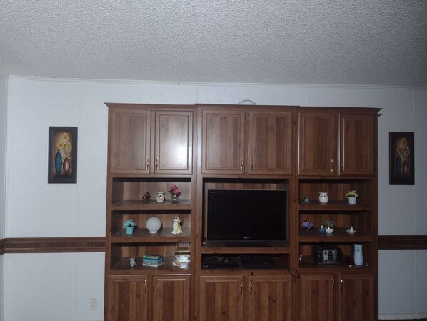Cozy living room with a flat-screen TV and entertainment center, featuring decorative items and a textured ceiling.
