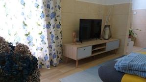 A modern bedroom with a TV on a wooden TV stand, a bed with a grey and yellow bedspread, and a potted plant.