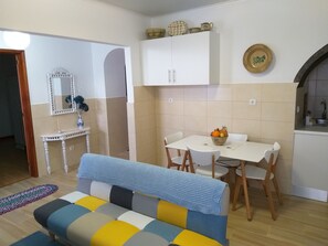 A compact living space with a sofa, dining table, and chairs. A white cabinet with decorative items is above the table.