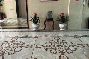 A lobby with a tiled floor, potted plants, and a chair. - Jingyue Boutique Hotel (Linyi Olympic Sports Center Store) (Linyi)
