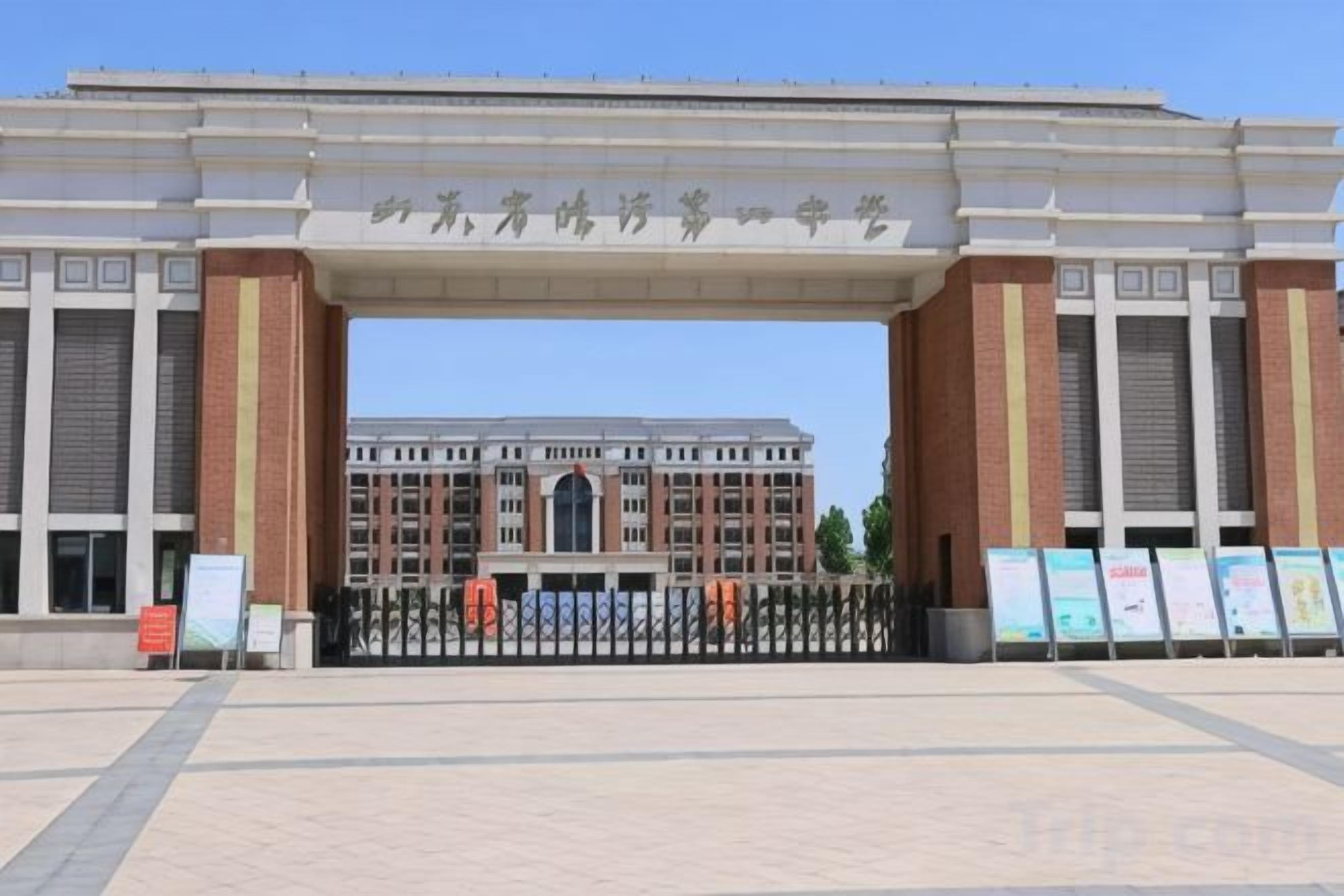 A large building with a prominent entrance archway, a paved plaza in front, and informational signs.