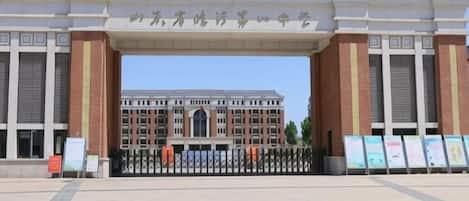 A large building with a prominent entrance archway, a paved plaza in front, and informational signs.