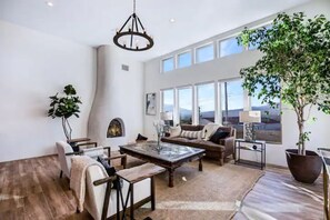 Relax in this spacious living room with a high ceiling and large windows offering a view of the outdoors. Enjoy a comfortable seating area with a sofa, chairs, and coffee table.