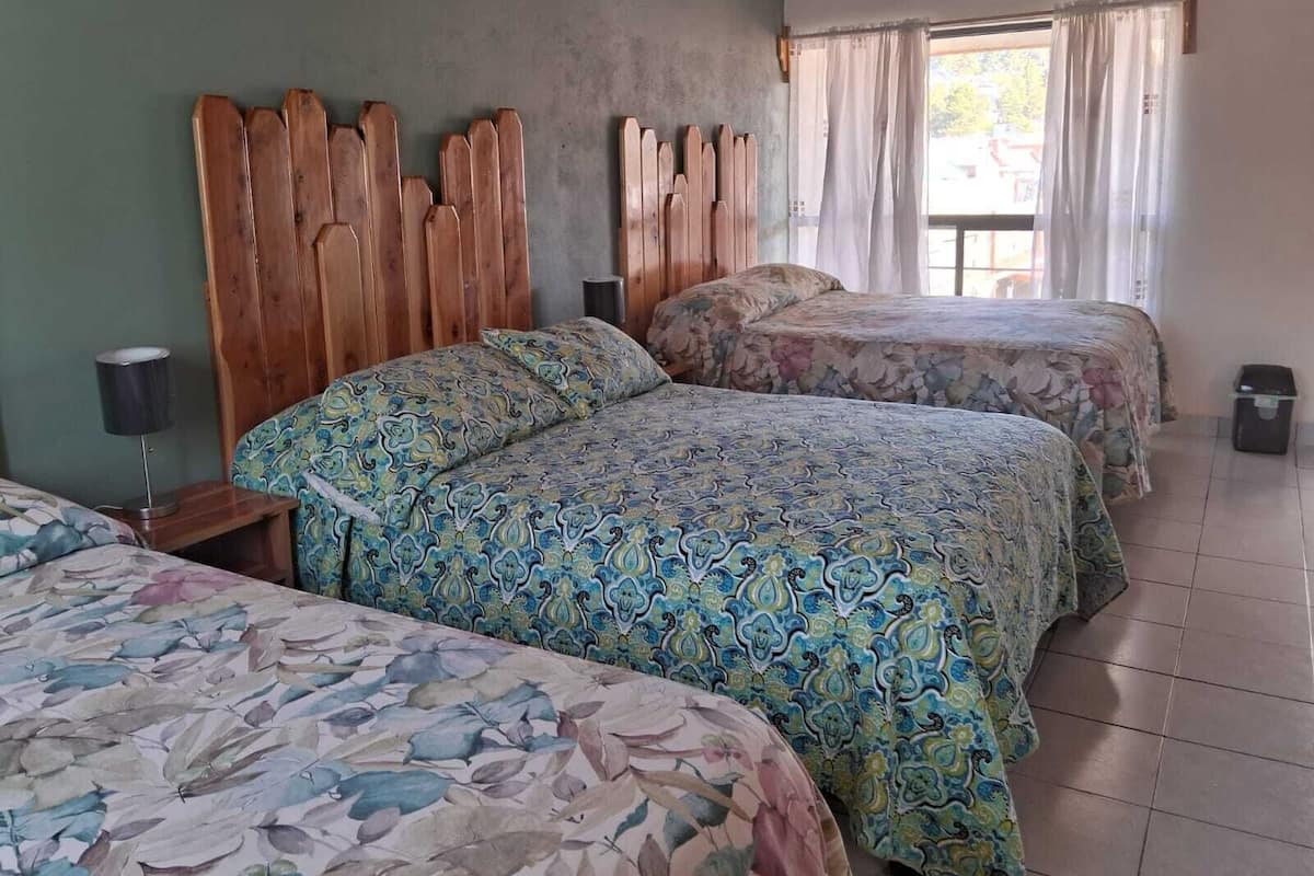 A hotel room with two beds, a wooden headboard, a nightstand with a lamp, and a window with curtains.
