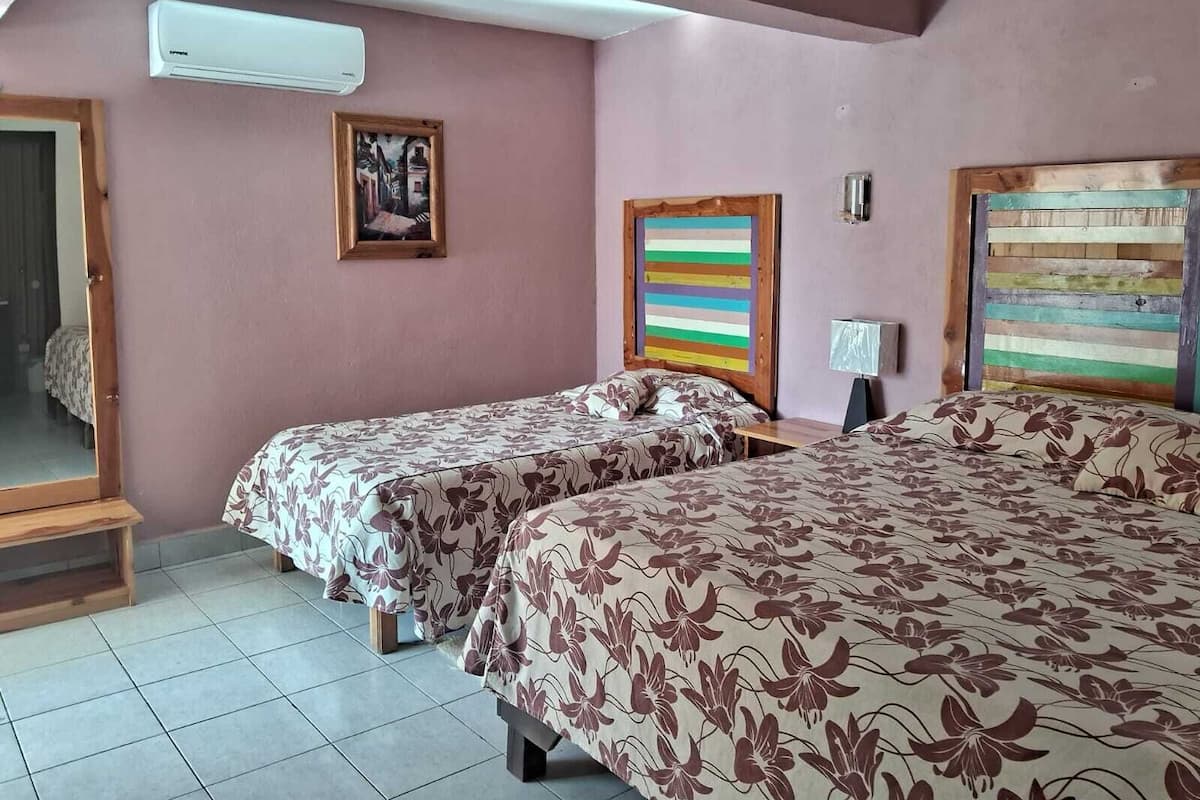 A room with two beds, a wooden headboard, a colorful striped wall art, a framed picture, and an air conditioning unit.