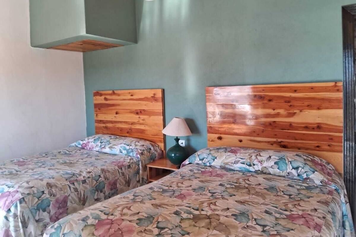 A room with two beds, each with floral-patterned bedding, wooden headboards, and a nightstand with a lamp.
