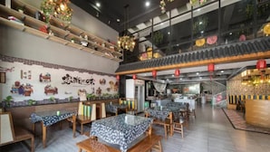 A restaurant with wooden tables and chairs, a kitchen area, and a decorative wall with traditional elements.